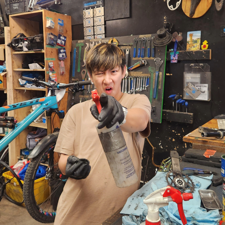 person in a bike repair shop making a funny face holding a squeeze bottle to the camera