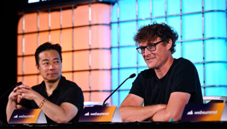 Ken Sim and Paddy Cosgrave sitting in front of a coloured background speaking at Web Summit Vancouver