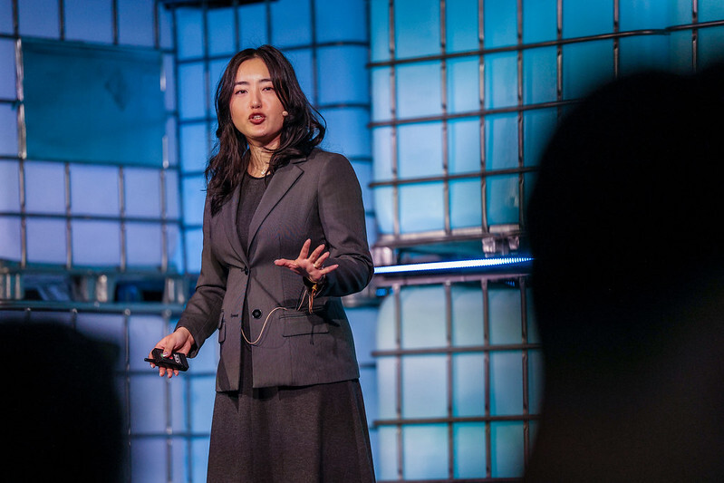 woman in a grey suit speaking on a stage at Web Summit Vancouver in front of a blue background