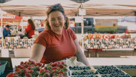Woman at farmers' market in front of stall with strawberries and blueberries