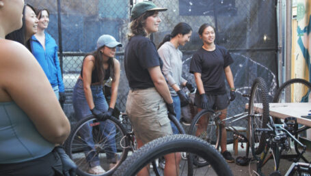 A ground of women and individuals standing around bikes behind a building