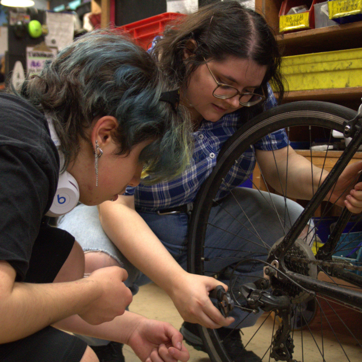 two people crouching around a bike tire adjusting it