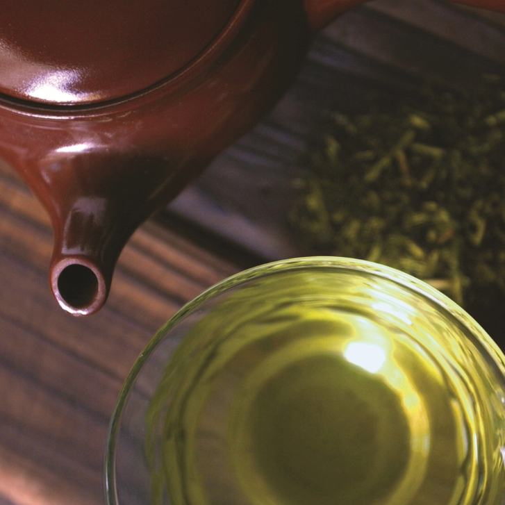 top view of a brown tea pot and a clear glass of green tea